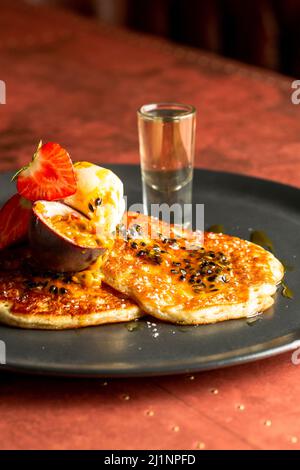 Un Closeup di pancake con fragole, un frutto della passione, e gelato servito su un piatto nero Foto Stock