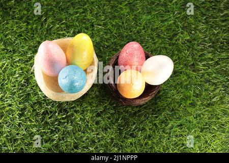 Due uova di Pasqua annidi ciascuno con tre uova colorate e scintillanti all'interno su uno sfondo di erba. Foto Stock