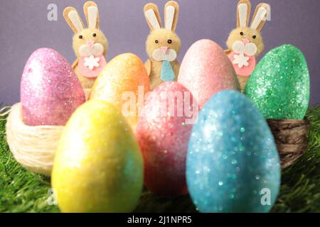 Tre coniglietti pasquali spaziati uniformemente dietro le uova di pasqua colorate su uno sfondo viola. Foto Stock