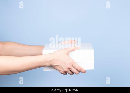 Donna che tiene la scatola di cartone bianco su sfondo azzurro. Pacco bianco vuoto. Imballaggio, shopping, concetto di consegna Foto Stock