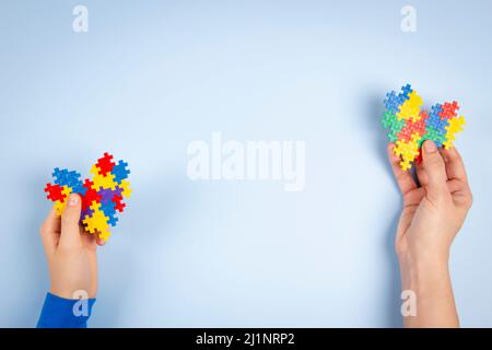 Concetto di giornata di consapevolezza autismo mondiale. Mano donna e mano bambino che tiene colorato cuore puzzle su sfondo azzurro chiaro Foto Stock