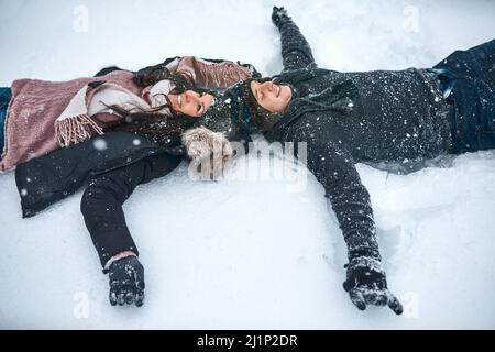 La neve ci fa sentire ancora come dei bambini. Colpo ad angolo alto di una coppia che si trova nella neve facendo angeli di neve. Foto Stock