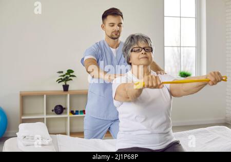Donna anziana con nastro elastico che fa esercizio di stretching con fisioterapista maschile. Foto Stock