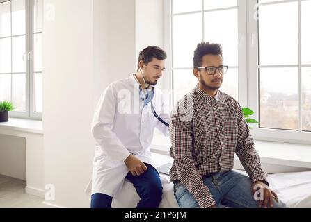 Medico che utilizza lo stetoscopio per controllare la respirazione o il battito cardiaco di un giovane paziente di sesso maschile Foto Stock