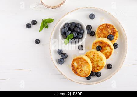 Formaggi caserchi o frittelle di cagliata con miele e mirtillo fresco. Dieta sana, colazione. Vista dall'alto. Foto Stock