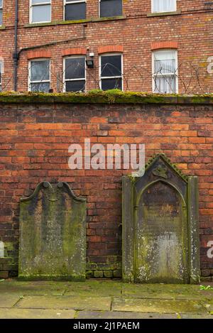 Vecchie lapidi poggiano contro vecchie mura di mattoni nella città inglese. Carlisle, Regno Unito. Foto Stock