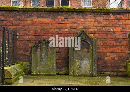 Vecchie lapidi poggiano contro vecchie mura di mattoni nella città inglese. Carlisle, Regno Unito. Foto Stock