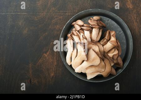 Funghi di ostrica freschi. Stira una vecchia ciotola di deliziosi funghi ostrica biologici su un vecchio sfondo di legno, vista dall'alto con spazio per il testo. Foto Stock