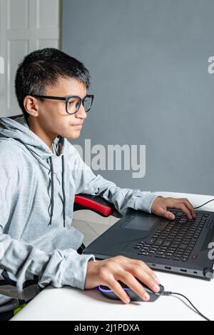 Teen adolager ragazzo casa scuola studiare stanza scrivania PC computer vetri seduta guardando i compiti Foto Stock