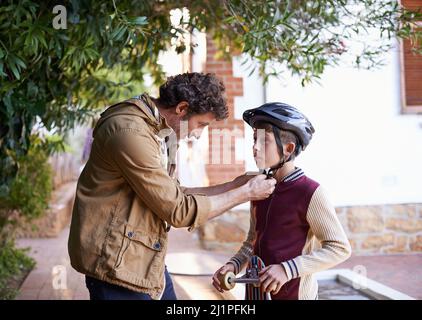 Sia sicuro fuori là figlio. Colpo di un padre che regola il casco dei suoi figli. Foto Stock