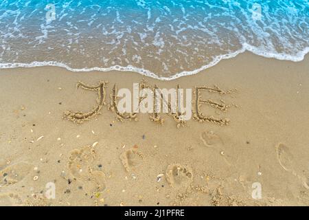 La parola giugno è scritta sulla sabbia di una spiaggia sul mare. Lavato via da un'onda. L'iscrizione scompare. Concetto di fine estate. Torna a scuola Foto Stock