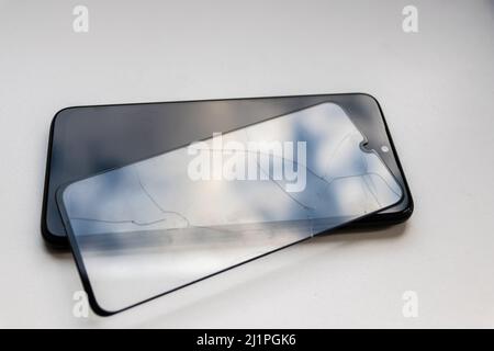 Lo schermo protettivo rotto su uno smartphone nero mostra la protezione del display e i dispositivi di protezione trasparenti infrangibili per la sicurezza contro gli urti dei telefoni cellulari Foto Stock