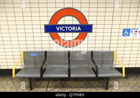 Londra, Inghilterra, Regno Unito. Piattaforma della stazione della metropolitana Victoria - roundel e posto a sedere Foto Stock