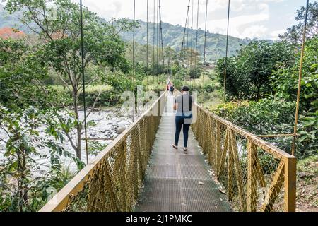 Persone che attraversano un fiume su un ponte sospeso nella valle di Orosi, Costa Rica. Foto Stock