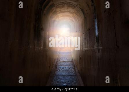 Tunnel scuro con sentiero stretto e fine del percorso che splende cielo e nuvole. Concetto di religione del paradiso o del paradiso. Foto Stock