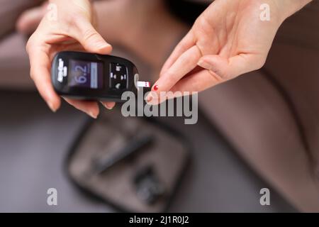 Analisi degli zuccheri nel sangue a casa. Donna che controlla il livello di zucchero nel sangue con glucometro e striscia di prova a casa. Diabetici che controllano i livelli di zucchero nel sangue. Foto Stock