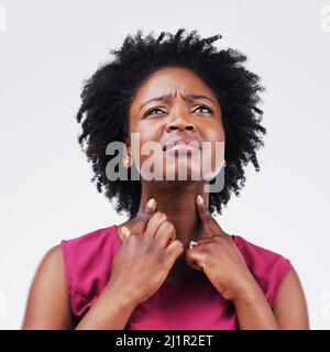 Mi chiedo che cosa potrebbe essere la causa di questo tanto dolore. Studio girato di una giovane donna che soffre con una gola dolorosa su uno sfondo grigio. Foto Stock