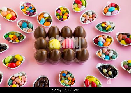 Uova di Pasqua decorative colorate in portauova trasparente su rosa con uova di cioccolato e caramelle di mandorle dolci e colorate in gusci d'uovo Foto Stock