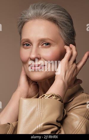 Ritratto di una bella donna anziana in un impermeabile beige con trucco classico e capelli grigi. Foto Stock