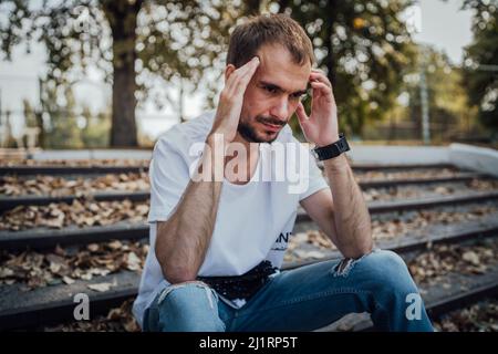 Un bell'uomo in depressione. L'ippico non rasato siede sui gradini del Parco autunnale tenendo la testa. Foto Stock