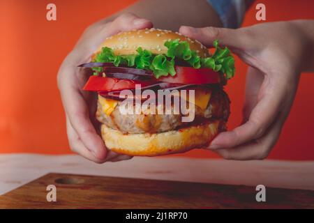 Le mani delle donne stanno tenendo un hamburger succosa enorme su sfondo arancione. Foto Stock