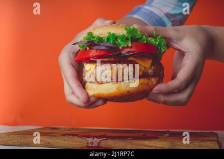Le mani delle donne stanno tenendo un hamburger succosa enorme su sfondo arancione. Foto Stock