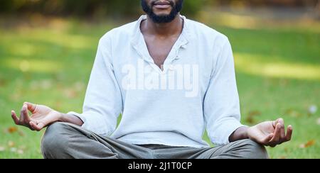 Sulla ricerca della pace interiore. Scatto corto di un giovane irriconoscibile meditando mentre si pratica lo yoga all'esterno del parco. Foto Stock