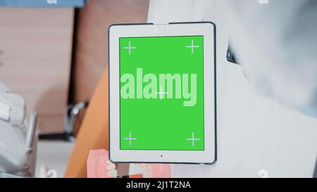Video verticale: Primo piano del dentista utilizzando lo schermo verde sul tablet per la cura del tè in ufficio di stomatologia. Ortodontista che lavora con chiave cromata e stampo mockup isolato sul dispositivo per la cura orale Foto Stock