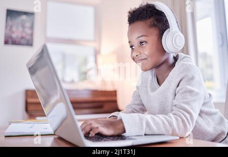 Chi ride di più, impara meglio. Scatto di un ragazzino che fa i compiti su un portatile a casa. Foto Stock