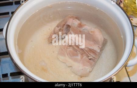 Un pezzo di carne cruda in una pentola bianca smaltata da vicino, cucinando brodo di carne fatto in casa. Foto Stock