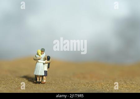 Fotografia di personaggi giocattolo in miniatura. Concetto di ricongiungimento familiare. Padre che abbraccia sua moglie e sua figlia nel deserto. Foto immagine Foto Stock