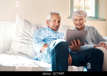 Abbracciare l'era della tecnologia intelligente. Scatto di una coppia anziana che usa un tablet digitale insieme nel salotto di casa. Foto Stock
