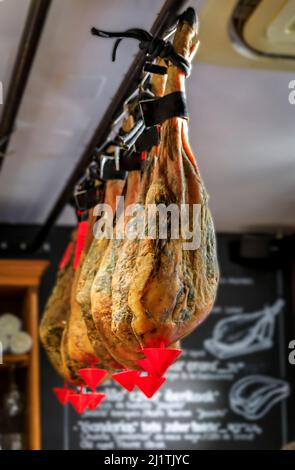 Intere zampe bone-in di prosciutto spagnolo serrano iberico in mostra presso un ristorante a San Sebastian Donostia, Paesi Baschi, Spagna Foto Stock