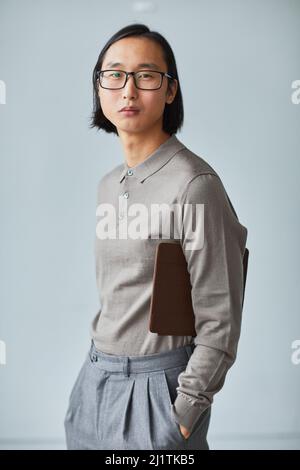 Ritratto verticale minimo del giovane uomo d'affari asiatico vestito in grigio su sfondo azzurro Foto Stock