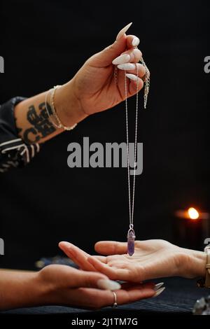 Vista laterale primo piano del cassiere di fortuna che tiene il cristallo magico sopra la mano della giovane donna e che legge il suo destino in seance spiritosa Foto Stock