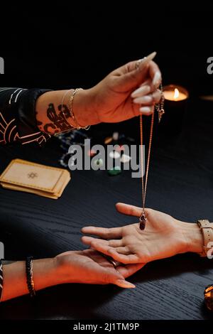 Primo piano verticale del cassiere di fortuna che tiene il cristallo magico sopra la mano della giovane donna e che legge il suo destino in seance spiritosa Foto Stock