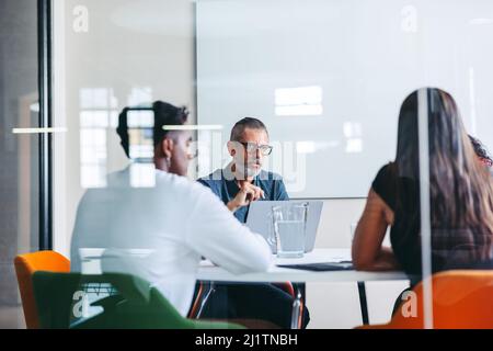 Gruppo di uomini d'affari che hanno una discussione in una sala riunioni. Uomo d'affari maturo con esperienza che conduce una riunione in un ufficio moderno. Gruppo di creativi Foto Stock