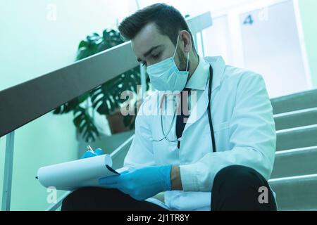 Giovane medico premuroso riempire il rapporto dopo un lungo turno Foto Stock