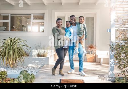 Le nostre vite sono benedette con tanto amore. Ritratto di una famiglia felice in piedi insieme fuori della loro casa. Foto Stock