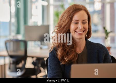 Donna d'affari che ride mentre lavora su un notebook in ufficio Foto Stock