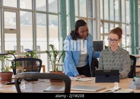 Due diverse donne d'affari che lavorano su un tablet alla scrivania dell'ufficio Foto Stock