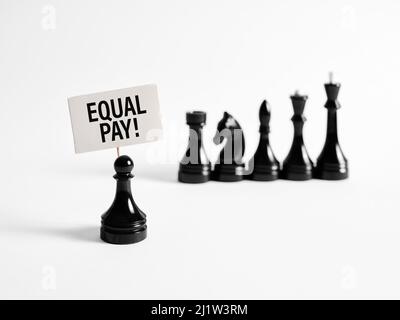 Chess pedone protester porta un banner con la parola pari retribuzione contro pezzi di scacchi più alto classificato. Parità di retribuzione per parità di lavoro. Foto Stock