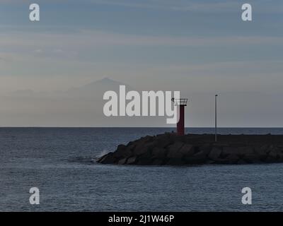 Vista di un faro al porto di la Aldea de San Nicolas sulla costa occidentale di Gran Canaria, Spagna con la sagoma dell'isola di tenero con Teide. Foto Stock