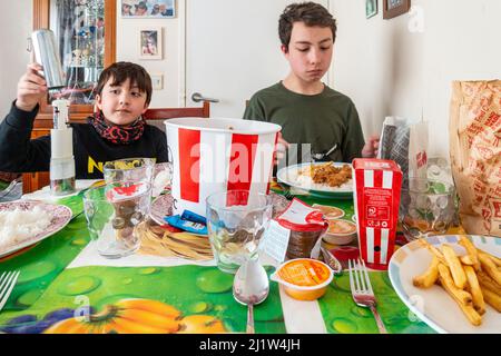 I fratelli si siedono al tavolo della sala da pranzo e gustano un pasto insieme, incluso il pollo fritto acquistato dal KFC. Foto Stock