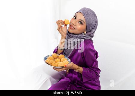 Una giovane signora malese con copertura testa celebra la fine del Ramadan, il mese santo islamico, vestito in colorato vestito tradizionale viola, tenendo torte Foto Stock