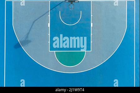 Vista dall'alto del canestro da basket posto sul terreno sportivo con superficie blu e linee nella soleggiata giornata estiva in città Foto Stock