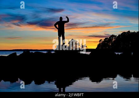 Silhouette di uomo in piedi forte di fronte al tramonto e al lago Foto Stock