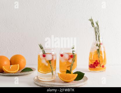 due tazze moderne sotto forma di lattina con una bevanda rinfrescante fredda di arancia e bacche, ciuffi di marina su un tavolo bianco Foto Stock