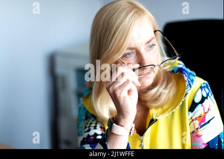 Primo piano ritratto di una donna pensierosa di mezza età seduta nella sua sedia da ufficio focalizzata sul lavoro Foto Stock