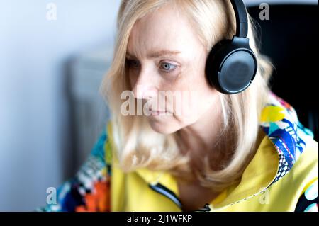 Primo piano di una donna di mezza età che indossa le cuffie guardando il webinar sul computer dell'ufficio Foto Stock